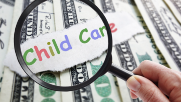 This image shows a person's hand holding a magnifying glass over the words "child care" with money in the background.